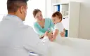 Pediatra bada niemowlę podczas pierwszej wizyty. Mama z uśmiechem obserwuje badanie.
