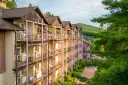 Hotel z balkonami w otoczeniu zieleni i gór.