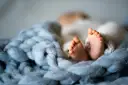 Malutkie stópki dziecka, rozmiar 74 sugeruje wiek około 6-9 miesięcy. Otulone w miękkie kocyki.
