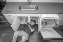 Mężczyzna pod zlewem sprawdza, jak sprawdzić elektrozawór w zmywarce, która jest otwarta.