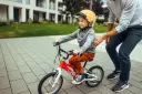 Chłopiec w kasku na rowerze, rozmiar 128, uczy się jeździć. Tata go asekuruje.