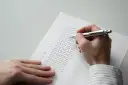 Dłoń z długopisem wypełnia ankietę z polami wyboru.