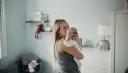 Mama tuli tulula noworodka, kołysząc go czule. W tle pokój dziecięcy z pluszakami.