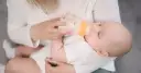 Mama karmi dziecko mlekiem modyfikowanym z butelki. Dziecko pije spokojnie, a mama czule go trzyma.