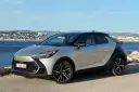 Srebrno-czarna Toyota C-HR na tle morza i miasta. Zastanawiasz się, ile przejedzie hybryda Toyoty na jednym ładowaniu?