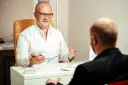 Lekarz psychiatra w białym kitlu rozmawia z pacjentem. Dyskutują o tym, ile zarabia lekarz psychiatra, analizując dane.