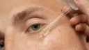 Nahaufnahme eines Auges, auf das ein Tropfen Öl aus einer Pipette aufgetragen wird.