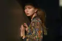 Justyna Wasilewska w kolorowej kurtce opiera się o ciemną ścianę, jej twarz oświetla cień.