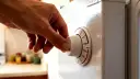 Dłoń kręci pokrętłem termostatu lodówki, ustawiając temperaturę.
