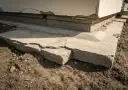 Popękane betonowe fundamenty domu, widoczne uszkodzenia i nierówności.