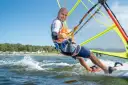 Mężczyzna na desce windsurfingowej, uśmiecha się i pokazuje kciuk w górę.