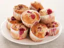 Stos muffinek z malinami na białym talerzu.