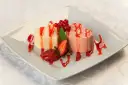 Dwie panna cotta w kształcie serc, polane sosem truskawkowym, ozdobione owocami i miętą.