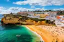 Coastal town with white buildings on cliffs overlooking a sandy beach and turquoise water.