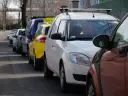 Rząd zaparkowanych samochodów, w tym żółty i biały, na ulicy.