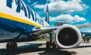 Fragment samolotu Ryanair z widocznym silnikiem i podwoziem na tle nieba.