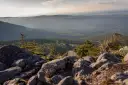 Widok z kamienistego szczytu na dolinę porośniętą lasem. W oddali widać zabudowania, być może schronisko sokolec, otoczone zielenią.