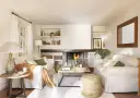 Salón acogedor con chimenea encendida, sofás blancos, mesa de centro de madera y detalles decorativos.