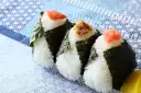 Trzy onigiri z ryżem, zawinięte w nori, z łososiem, tuńczykiem i ikrą na wierzchu. Idealne na przekąskę.
