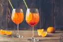 Dwa orzeźwiające drinki Aperol z plastrami pomarańczy i słomkami, na drewnianym stole.
