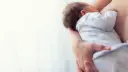 Ciepłe objęcia mamy, maluszek karmiony piersią. Delikatne dłonie otulają dziecko, tworząc bezpieczną przestrzeń.