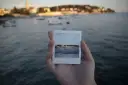 Dłoń trzyma zdjęcie z widokiem na zatokę z łodziami, jak wywoływanie zdjęć jak z instaxa.
