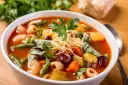 A miseczce aromatyczna zupa minestrone, oryginalny przepis z makaronem, fasolką, ziemniakami i startym parmezanem.