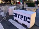 Betonowe bariery NYPD na ulicy. Czy w USA jest bezpiecznie? Widać ludzi i ruch uliczny w tle.