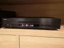 Czarny odtwarzacz CD Yamaha CD-S303 na drewnianej półce, gotowy do testu. Wyświetlacz pokazuje utwór 10 z 2:08.