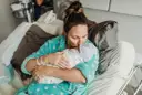 Mama tuli dziecko po cesarce, czule całując je w czapeczkę. Laktacja po cesarce może być wyzwaniem, ale miłość jest silniejsza.