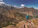 Widok na ośnieżone szczyty górskie Jebel Toubkal. Turystka podziwia panoramę z skalistego zbocza.