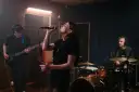Wokalistka z pasją śpiewa w zespole, podczas gdy gitarzysta i perkusista tworzą rytm w studiu nagraniowym.
