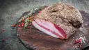 Guanciale co to? Włoski, peklowany policzek wieprzowy, pokryty pieprzem, leży na drewnianej desce z ziołami i pieprzem.