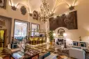 Elegant hotel lounge with a bar, fireplace, ornate chandelier, and artwork.