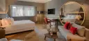 Modern hotel room with a bed, sofa, desk, and large round mirror reflecting the room.