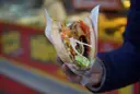 Kebab w bułce z warzywami i mięsem, trzymany w dłoni.