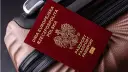 Czerwony paszport Polski z godłem orła leży na brązowej walizce.