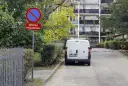 Znak zakazu postoju i tabliczka "Droga pożarowa" obok białego vana zaparkowanego przy chodniku.