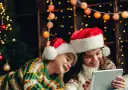 Dos niños con gorros de Santa Claus disfrutan de la tablet, felices cuando dan vacaciones de Navidad, rodeados de luces festivas y un árbol.