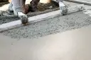 Ręce w rękawiczkach wyrównują świeży beton na taras za pomocą łaty.