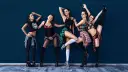 Pięć kobiet w stylizacjach do sexy dance, w ruchu, na tle granatowej ściany.