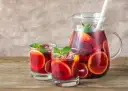 Dwa szklanki i dzbanek pełne orzeźwiającej Sangrii czerwonej z plasterkami pomarańczy i limonki, ozdobione miętą. Idealny wybór na lato!