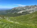 Widok na Tatry z zielonymi zboczami i skalistymi szczytami. W oddali widać budynki. Zastanawiasz się, ile km jest na Kasprowy Wierch?