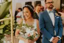 Szczęśliwa panna młoda z bukietem kwiatów i pan młody w niebieskim garniturze podczas ceremonii ślubnej.