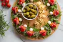 Kolorowe przekąski na desce: szaszłyki z pomidorkami, mozzarellą, salami i rukolą, oliwki i serowe zawijasy. Idealne finger food na imprezę.