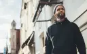 Mężczyzna w czarnej bluzie z kapturem i czapce beanie patrzy w górę. Stylowy sposób, jak nosić bluzę z kapturem.