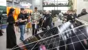 Ludzie zwiedzają targi energii odnawialnej, oglądając panele słoneczne i stoiska firm.