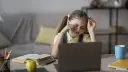 Zmęczona dziewczynka z okularami na czole pociera oczy, ucząc się przy laptopie. Jej indywidualna ścieżka nauczania jest trudna.