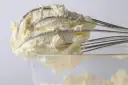 Puszysty krem z mascarpone, ubijany na drucianych trzepaczkach miksera, gotowy do deseru.