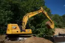 Żółta koparka Cat 313 z łyżką pełną ziemi, gotowa do pracy. Dane techniczne tej maszyny budowlanej są imponujące.